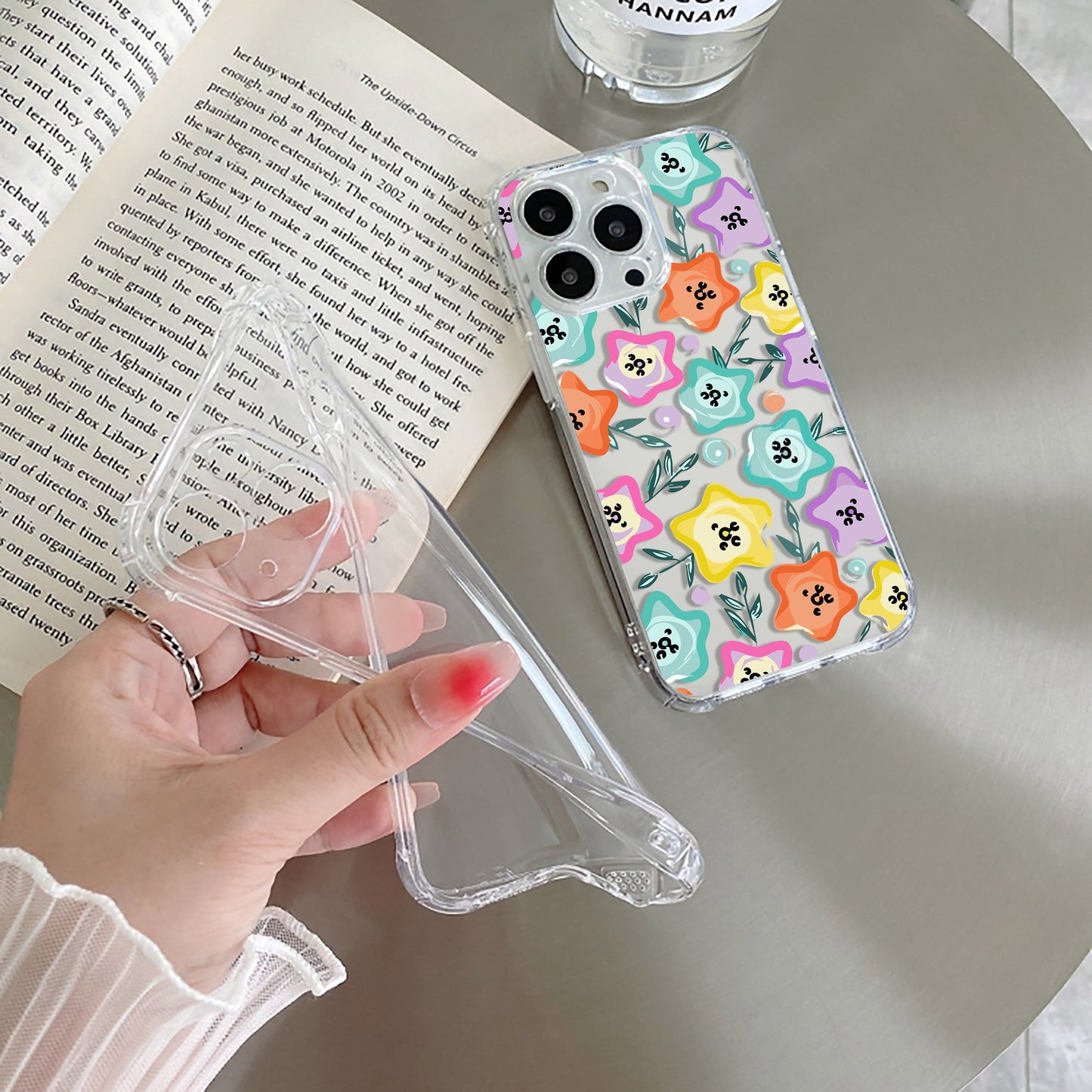 A transparent silicone mobile phone case with a whimsical star-shaped flower design in a lively rainbow palette, held in a person's hand.