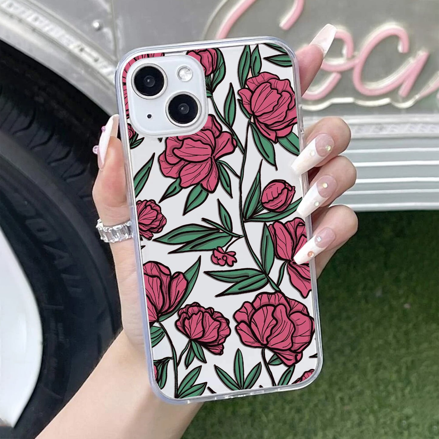 Phone case with pink floral design held by a hand, blurred background