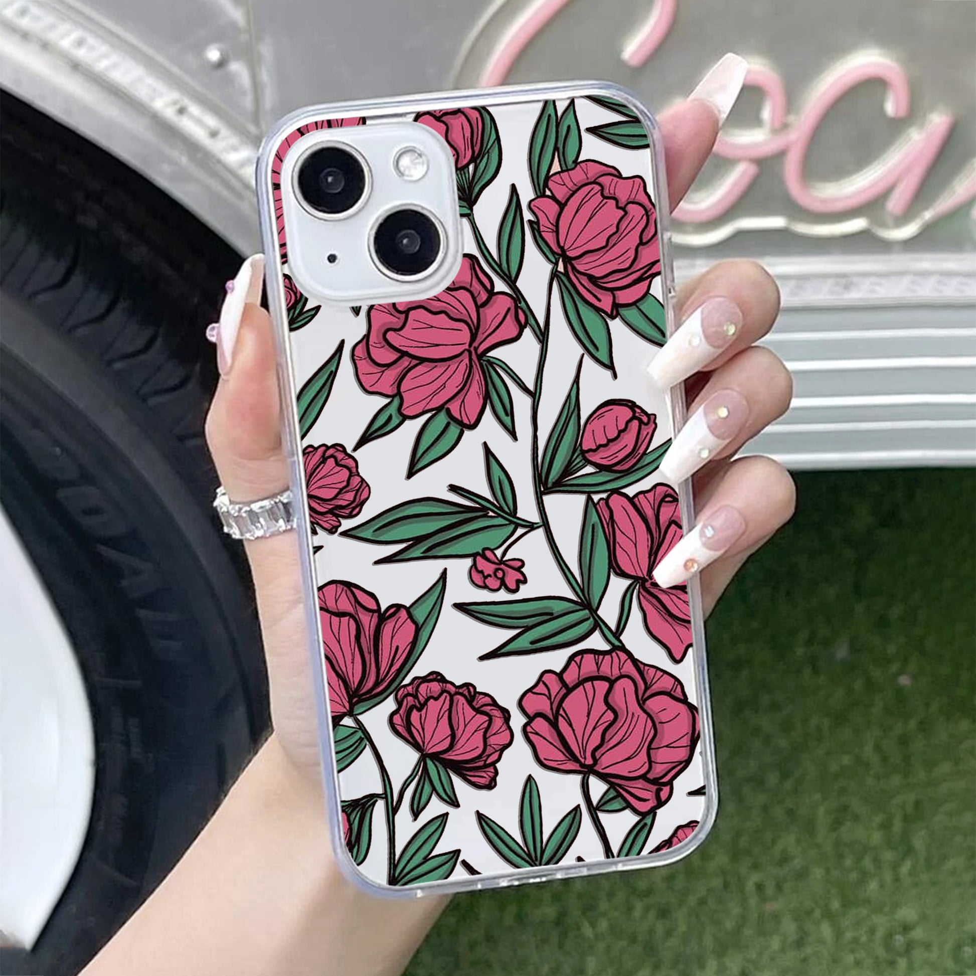 Phone case with pink floral design held by a hand, blurred background