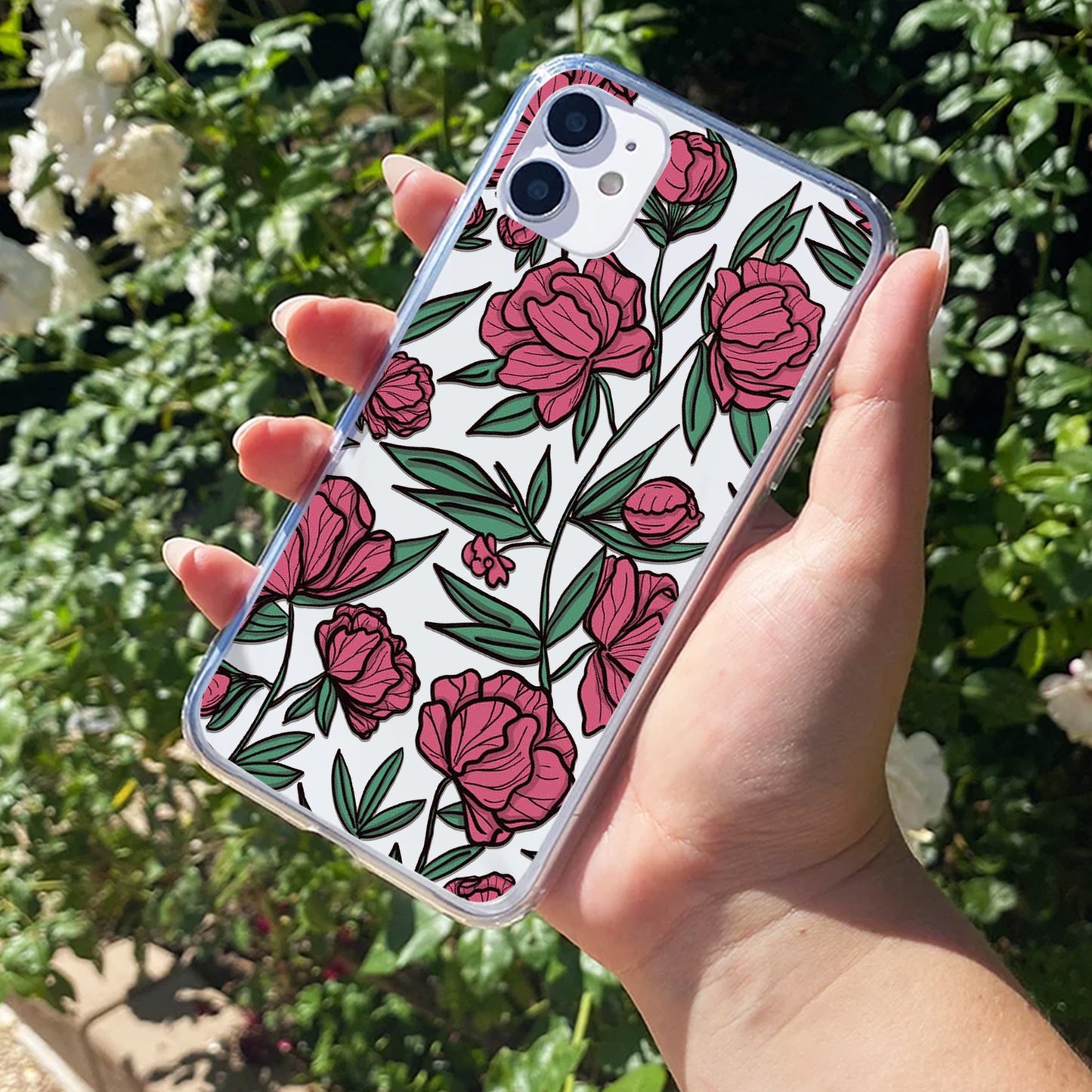 Phone case with pink floral design held by a hand against a green outdoor background
