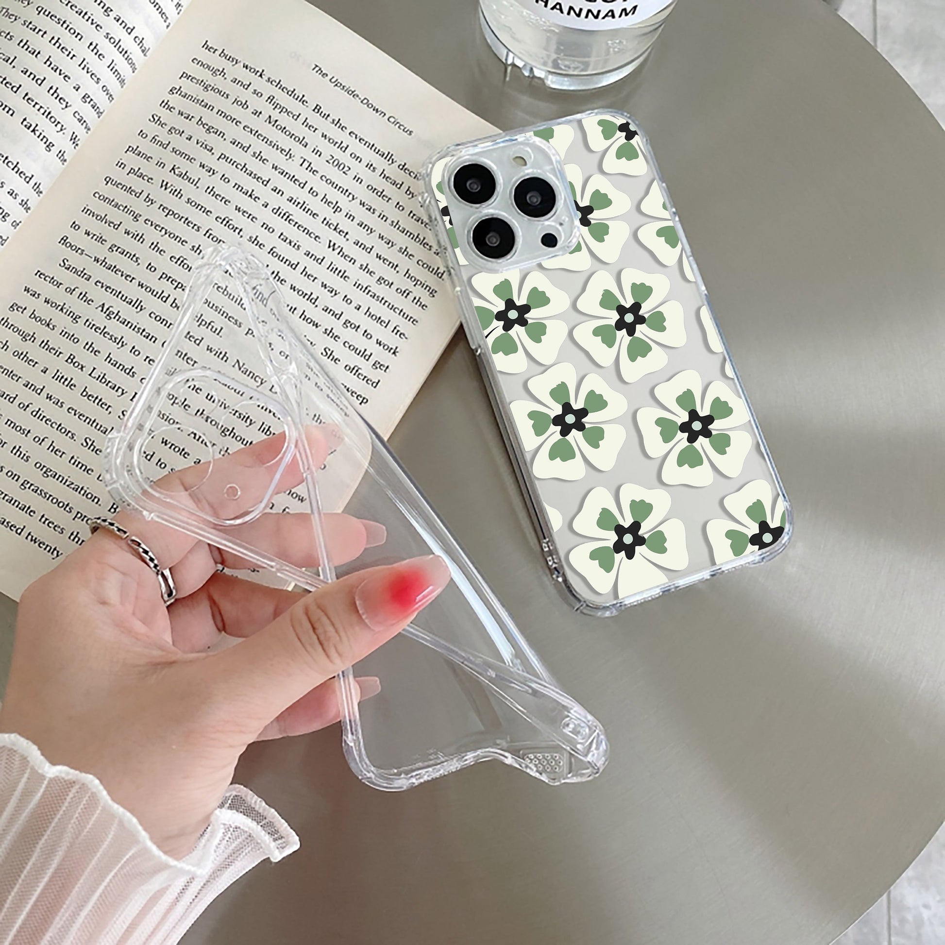 A transparent silicone mobile phone case with a black and green flower pattern, held in a person's hand.