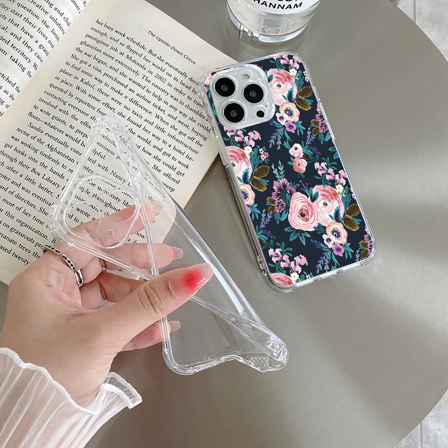 A transparent silicone phone case with a floral pattern in soft pink, purple, and green on a dark background, held in a person's hand.