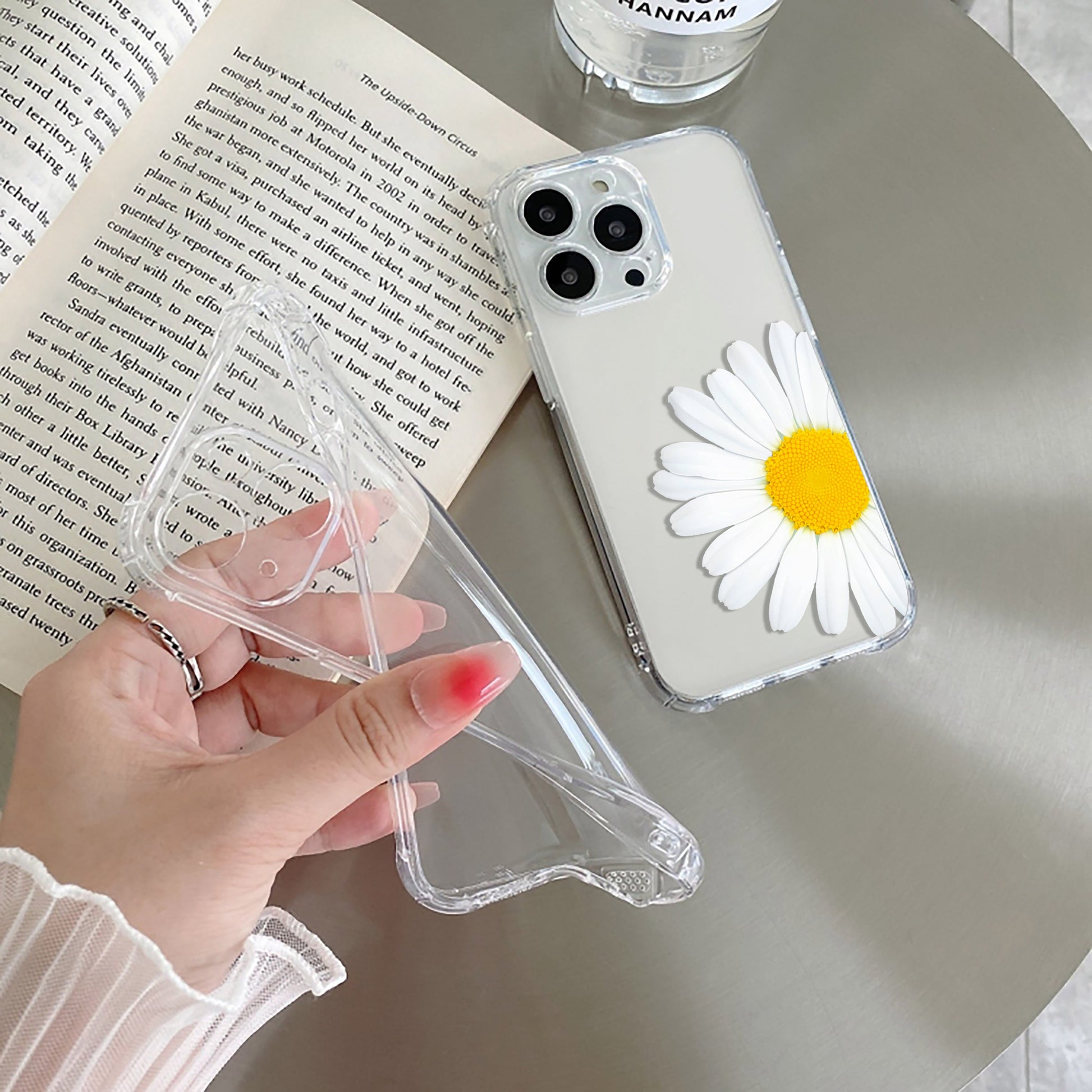 A transparent silicone mobile phone case with a daisy flower design on the back, held in a person's hand.