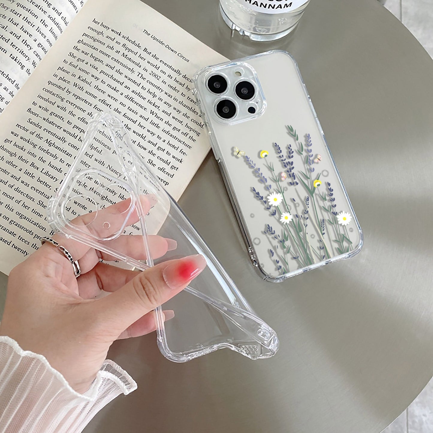 Hand holding a phone case with floral design next to an open book on a table.