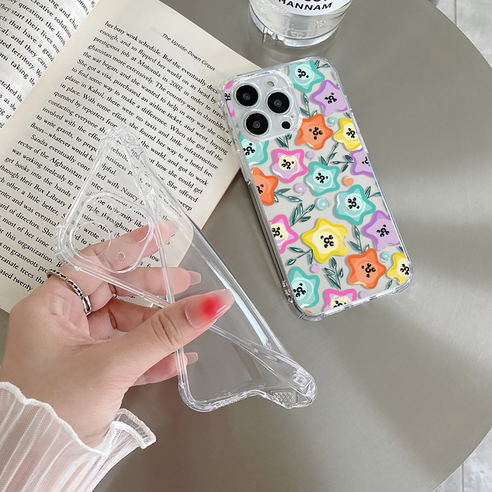 A transparent silicone mobile phone case with a whimsical star-shaped flower design in a lively rainbow palette, held in a person's hand.